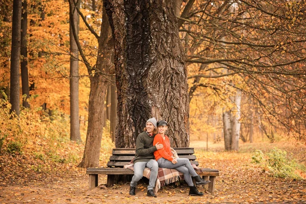 Молодая пара, сидящая на скамейке в осеннем парке — стоковое фото