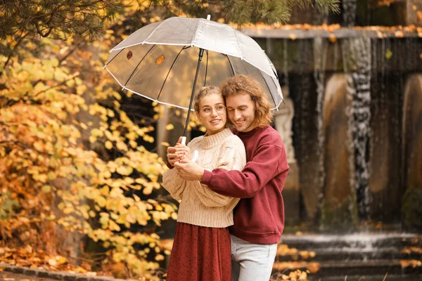 Young couple with umbrella in park on autumn day — Stock Photo, Image