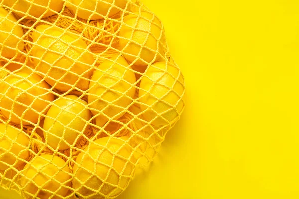 Sac en maille avec citrons mûrs sur fond de couleur — Photo