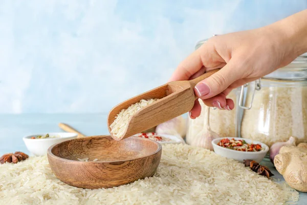 Woman pouring raw rice from scoop onto plate on table — Stock Photo, Image