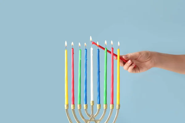 Woman lighting candles in menorah for Hanukkah on color background — Stock Photo, Image