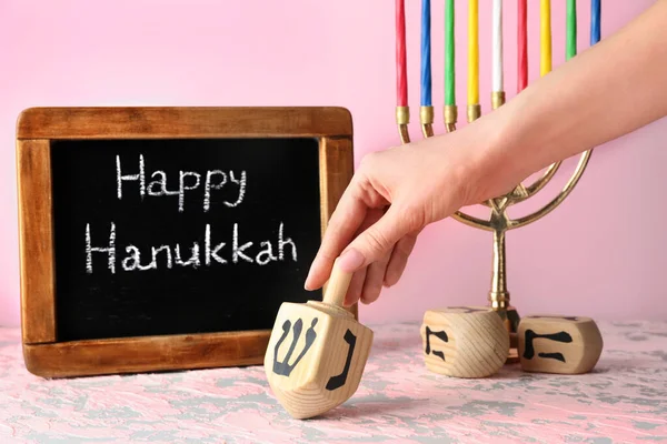 Vrouwelijke hand met dreidel, menorah en schoolbord met tekst Happy Hanukkah op tafel — Stockfoto