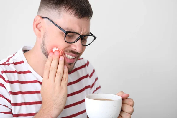 Man with sensitive teeth and hot coffee on light background