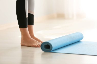 Evde yoga minderinin yanında duran genç bir kadın.