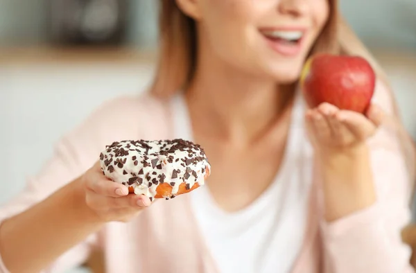 Woman with healthy apple and unhealthy donut in kitchen. Diet concept — Stock Photo, Image