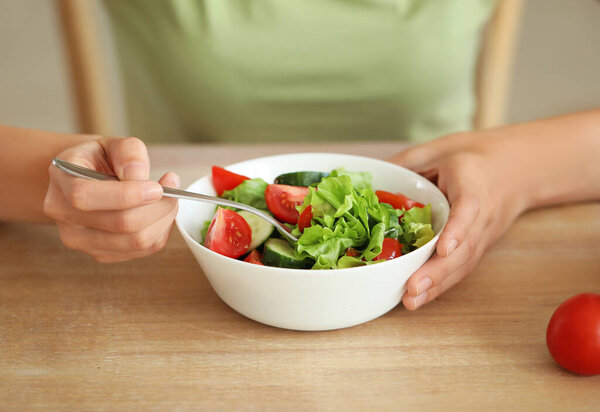 Young woman eating healthy vegetable salad in kitchen, closeup. Diet concept