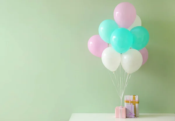 Luftballons mit Geschenkboxen auf dem Tisch vor farbigem Hintergrund — Stockfoto