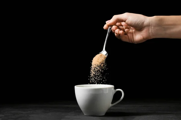 Nő öntés cukor kanál csészébe sötét háttér — Stock Fotó