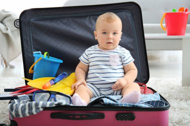 Evinde bavulu ve eşyaları olan sevimli bir bebek.