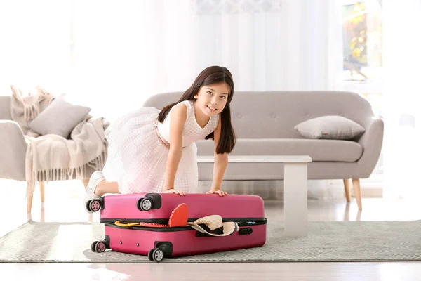 Cute girl trying to pack suitcase at home — Stock Photo, Image