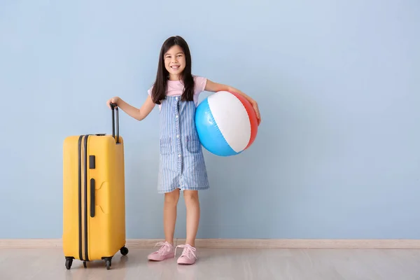 Cute girl with suitcase and inflatable ball near color wall — Stock Photo, Image