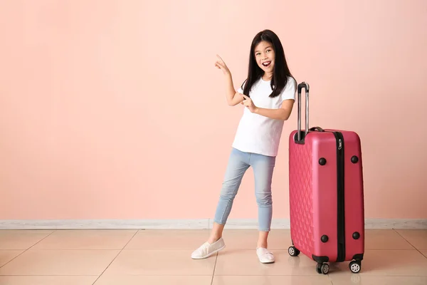 Cute girl with suitcase pointing at something near color wall — Stock Photo, Image