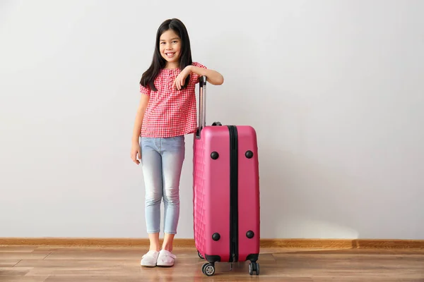 Cute girl with suitcase near light wall — Stock Photo, Image