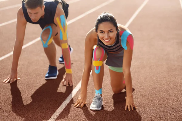 Couple sportif avec bande physio en position de départ accroupi au stade — Photo