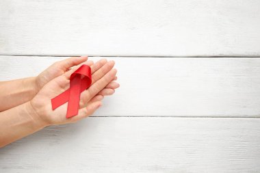 Beyaz ahşap arka planda kırmızı kurdeleli kadın eller. Yardım farkındalığı kavramı