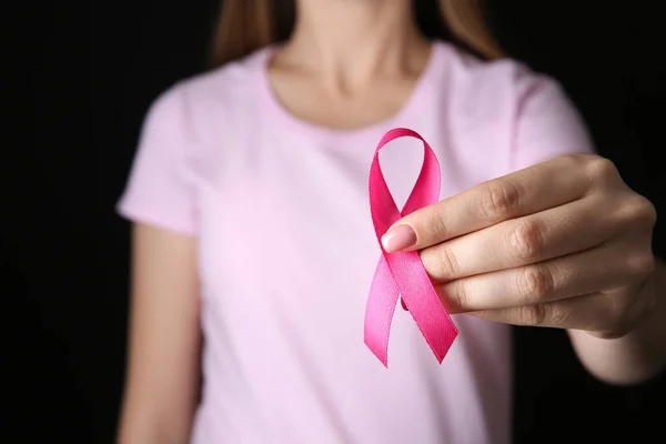 Young woman with pink ribbon on dark background, closeup. Cancer awareness concept — Stock Photo, Image