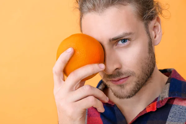 Portrait of handsome man with orange fruit on color background — Stock Photo, Image
