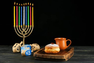 Menorah, donut for Hanukkah and dreidels on table against dark background clipart
