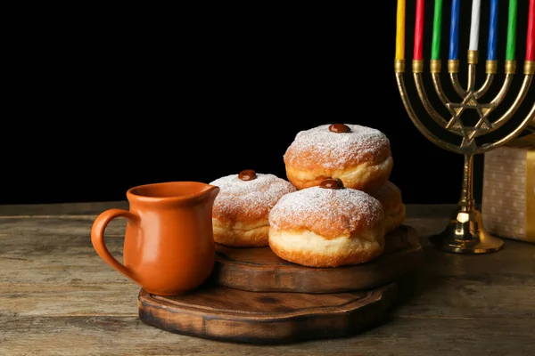 Menorah and donuts for Hanukkah on table against dark background — Stock Photo, Image