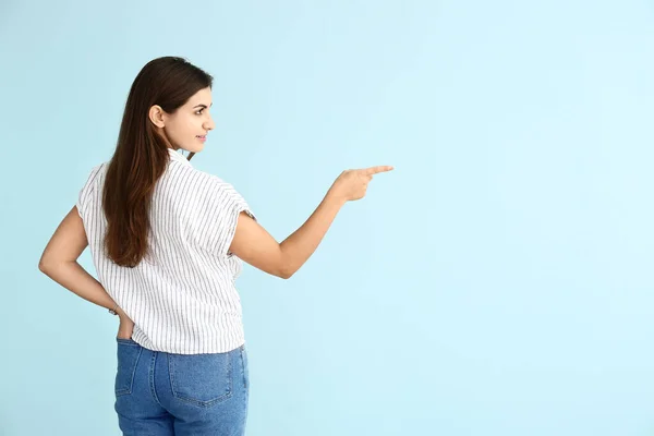 Beautiful young woman showing something on color background — Stock Photo, Image