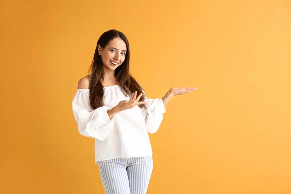 Mooie jonge vrouw tonen iets op kleur achtergrond — Stockfoto