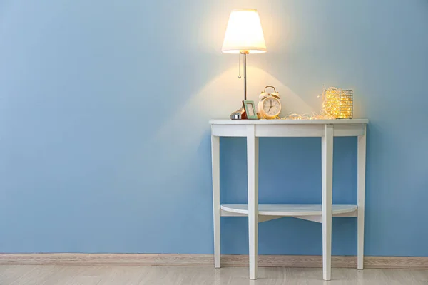 Beautiful glowing garland with alarm clock and lamp on table near color wall — Stock Photo, Image