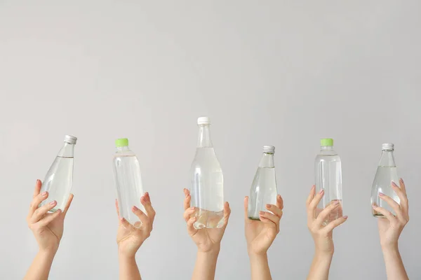 Frauenhände mit Wasserflaschen auf grauem Hintergrund — Stockfoto