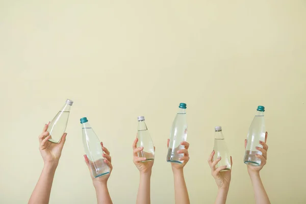 Weibliche Hände mit Wasserflaschen auf farbigem Hintergrund — Stockfoto