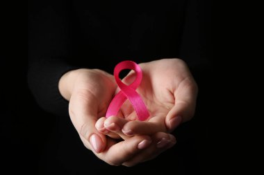 Koyu arkaplanda pembe kurdeleli kadın elleri. Kanser farkındalığı kavramı