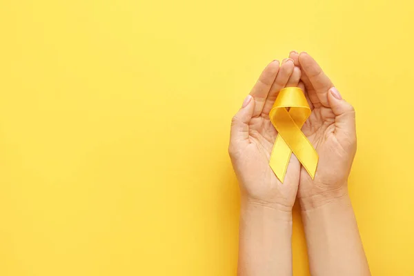 Жіночі руки з жовтими стрічками на кольоровому фоні. Концепція обізнаності про рак — стокове фото