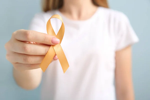 Young woman with golden ribbon on grey background, closeup. Cancer awareness concept — Stock Photo, Image