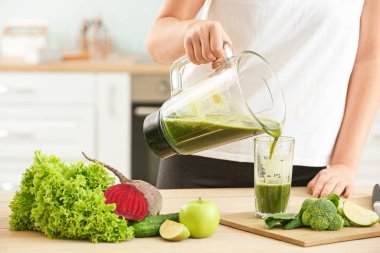 Kadın mutfaktaki cama sağlıklı meyve suyu döküyor.