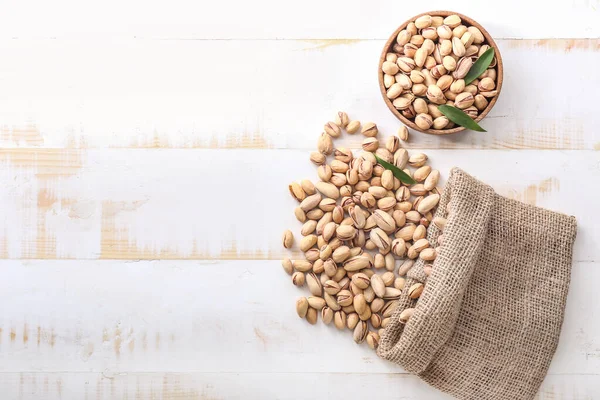 Bowl and bag with tasty pistachio nuts on table — Stock Photo, Image