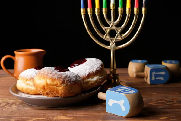 Menorah, dreidels and donuts for Hanukkah on table against dark background — Stock Photo, Image