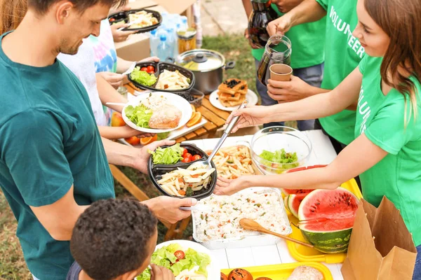 Young volunteers giving food to poor people outdoors