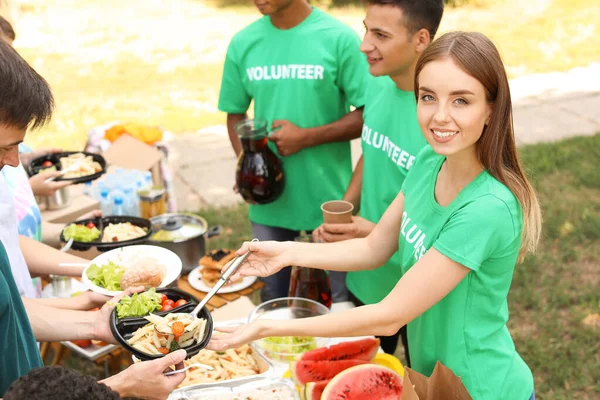 Jóvenes voluntarios dando comida a los pobres al aire libre — Foto de Stock