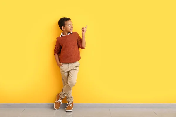 Fashionable African-American boy in autumn clothes pointing at something while standing near color wall — Stock Photo, Image