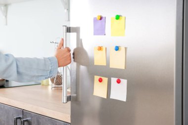 Mutfakta kapısında çıkartmalar olan modern buzdolabı açan bir kadın.