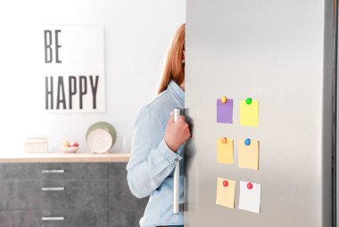 Mutfakta kapısında çıkartmalar olan modern buzdolabı açan bir kadın.