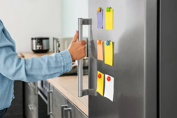 Woman opening modern fridge with stickers on door in kitchen — Stock Photo, Image