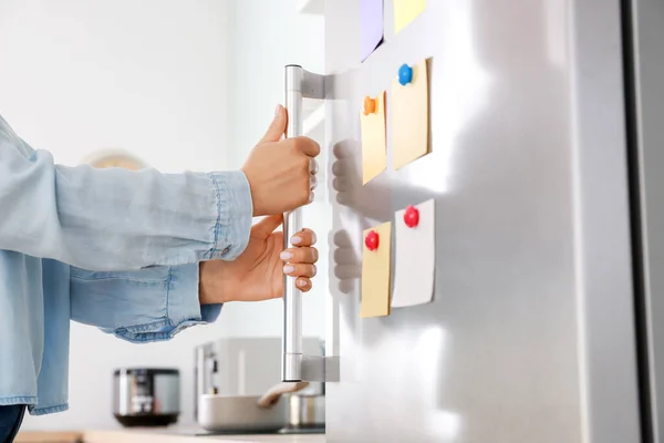 Mulher abrindo frigorífico moderno com adesivos na porta na cozinha — Fotografia de Stock