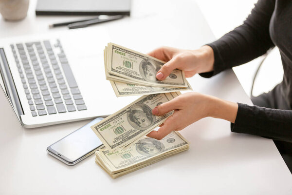 Женщина считает долларовые купюры за столом
