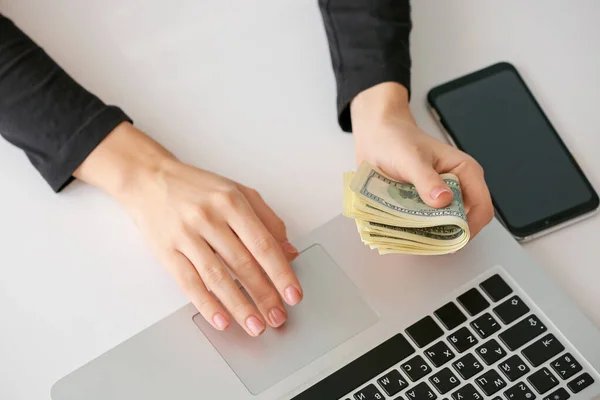 Kvinna med dollarsedlar med bärbar dator vid bordet — Stockfoto