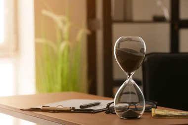 Masanın üzerinde dolar banknotları ve kırtasiye malzemeleri olan kum saati.