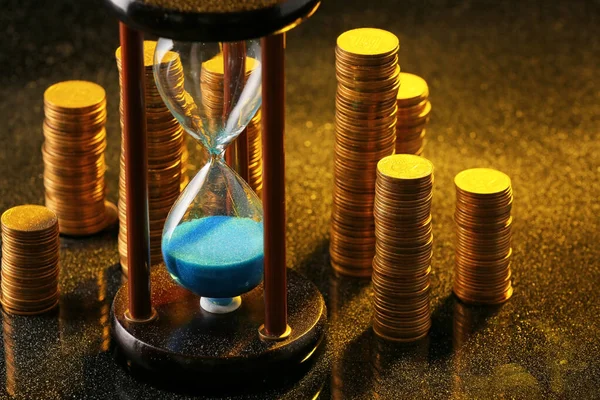 Hourglass with coins on dark background — Stock Photo, Image