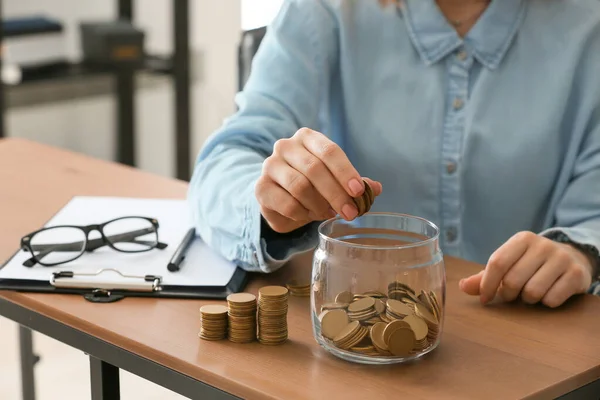 Kvinnan lägger mynt i burk på bordet. Koncept för penningbesparingar — Stockfoto