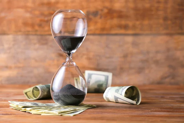 Crystal hourglass with dollar banknotes on wooden background — Stock Photo, Image