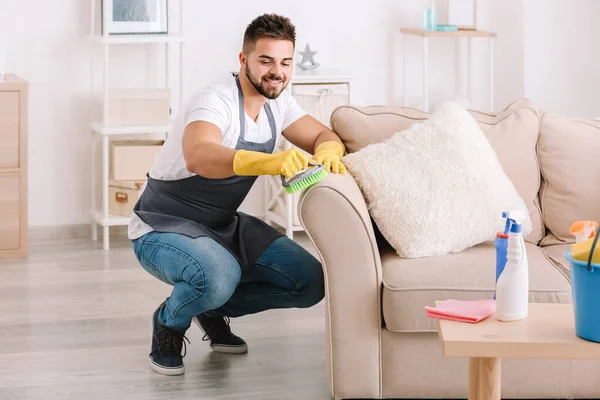Male janitor cleaning furniture in room — Stock Photo, Image