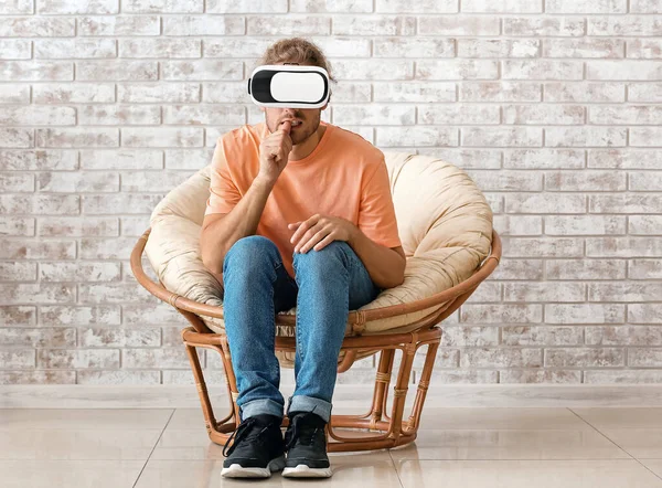 Giovane uomo con occhiali VR seduto vicino al muro di mattoni — Foto Stock