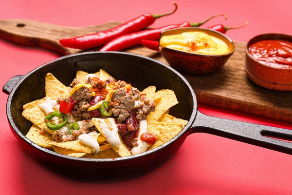 Padella con gustoso peperoncino con carne e nachos su sfondo colore — Foto Stock